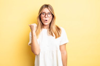 Sarışın, güzel bir kadın inançsızlıktan şaşkın şaşkın bakıyor, yan taraftaki objeyi işaret ediyor ve 