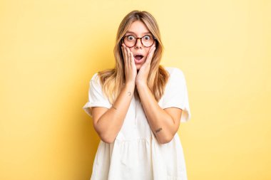 Sarışın, güzel bir kadın şok olmuş ve korkmuş hissediyor, ağzı açık ve elleri yanaklarında korkmuş görünüyor.