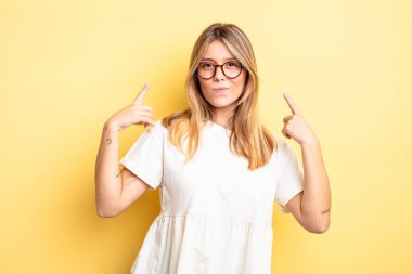 Sarışın, kötü tavırlı, gururlu ve agresif görünen, yukarıyı gösteren ya da elleriyle alay eden güzel bir kadın.