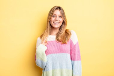 Sarışın, güzel bir kadın gururlu, kendinden emin ve mutlu görünüyor, gülümsüyor ve kendini işaret ediyor ya da bir numara işareti yapıyor.