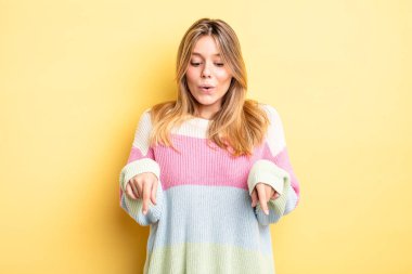 Sarışın, güzel bir kadın, ağzı açık, iki eliyle aşağıya bakıyor, şaşkın, şaşkın ve şaşırmış görünüyor.