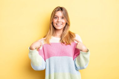 Sarışın, güzel, gururlu, pozitif ve iki elinle göğsünü gösteren bir kadın.