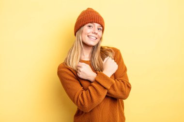 Sarışın, güzel bir kadın, neşeli bir şekilde gülümsüyor ve kutluyor, yumruklarını sıkıp kollarını kavuşturuyor, mutlu ve pozitif hissediyor.