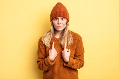 Sarışın, güzel bir kadın kendini işaret ediyor. Şaşırmış ve şaşırmış bir şekilde bakıyor.