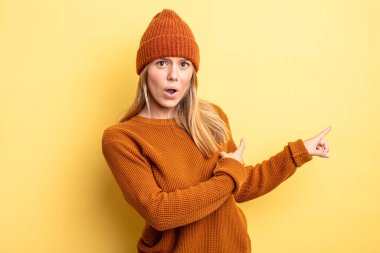 Sarışın, güzel bir kadın şaşkın ve şaşırmış hissediyor. Kenardaki fotokopi alanını işaret ediyor. Şaşırmış, ağzı açık bir bakış.