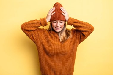 Sarışın, güzel bir kadın stresli ve hayal kırıklığına uğramış hissediyor, ellerinizi havaya kaldırıyor, yorgun, mutsuz ve migren ağrısı çekiyor.