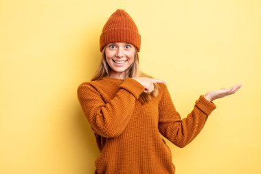 Sarışın, güzel bir kadın neşeyle gülümsüyor ve bir objeyi gösteren veya reklamını yapan avuç içindeki fotokopi alanını işaret ediyor.