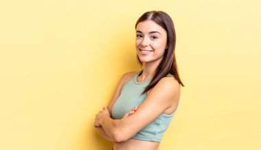 İspanyol asıllı güzel bir kadın kameraya çapraz kollarıyla gülümsüyor ve mutlu, kendinden emin, tatmin olmuş bir yüz ifadesi var.