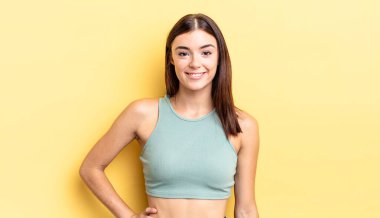 İspanyol güzel kadın mutlu bir şekilde gülümsüyor, eli kalçasında ve kendinden emin, olumlu, gururlu ve arkadaş canlısı.