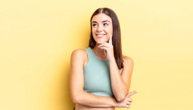 İspanyol güzel kadın mutlu bir şekilde gülümsüyor ve hayal kuruyor ya da şüphe ediyor, yan tarafa bakıyor.