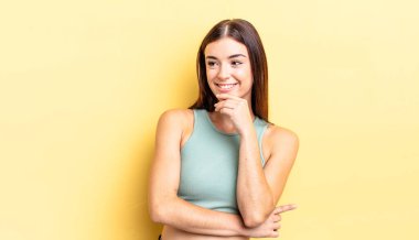 İspanyol güzel bir kadın mutlu, kendinden emin bir ifadeyle gülümsüyor. Elleri çenesinde, merak ediyor ve yan tarafa bakıyor.