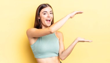 İspanyol güzel kadın gülümsüyor, mutlu, pozitif ve tatmin olmuş hissediyor, fotokopi alanında nesne ya da konsept tutuyor ya da gösteriyor