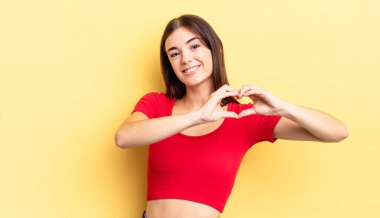 İspanyol güzel kadın gülümsüyor ve mutlu, sevimli, romantik ve aşık, iki eliyle kalbi şekillendiriyor.