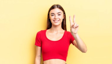 İspanyol güzel kadın gülümsüyor ve arkadaş canlısı görünüyor. İki ya da iki numarayı gösteriyor. Elleri önde, geriye doğru sayıyor.