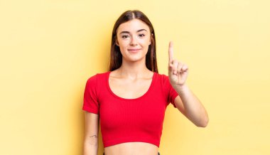 İspanyol güzel kadın gülümsüyor ve arkadaş canlısı görünüyor, bir numarayı gösteriyor ya da ilk eli önde, geri sayıyor.