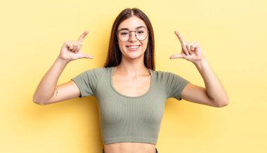 İspanyol asıllı güzel bir kadın iki eliyle kendi gülüşünü çiziyor, olumlu ve mutlu görünüyor, sağIık kavramı.