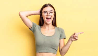 İspanyol güzel bir kadın gülüyor, mutlu, pozitif ve şaşırmış görünüyor, yanal fotokopi alanını işaret eden harika bir fikrin farkına varıyor.