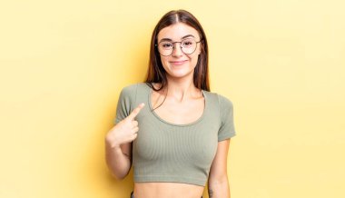 İspanyol güzel kadın gururlu, kendinden emin ve mutlu görünüyor, gülümsüyor ve kendini işaret ediyor ya da bir numara işareti yapıyor.