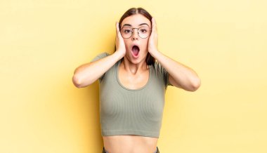 İspanyol güzel kadın hoş olmayan bir şekilde şok olmuş, korkmuş ya da endişeli görünüyor, ağzı sonuna kadar açık ve iki kulağını da elleriyle kapatıyor.