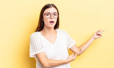 İspanyol güzel kadın şaşkın ve şaşkın hissediyor, kenarda fotokopi alanını işaret ederek, şaşkın, açık ağızlı bir görünüm ile