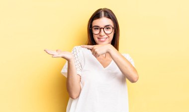 İspanyol güzel kadın neşeyle gülümsüyor ve yan taraftaki fotokopi alanını işaret ediyor, bir nesneyi gösteriyor ya da reklamını yapıyor.