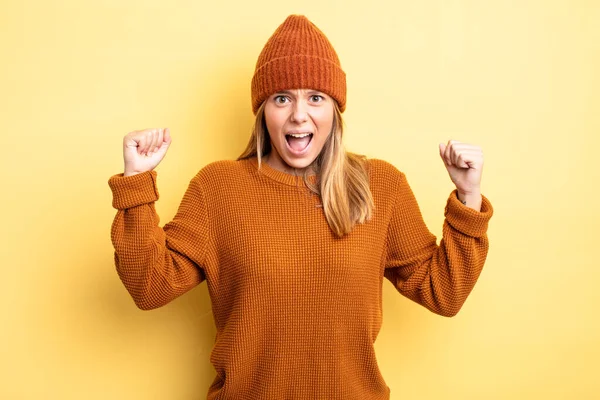 Sarışın, güzel bir kadın sinirli bir ifadeyle bağırıyor ya da yumruklarıyla başarıyı kutluyor.