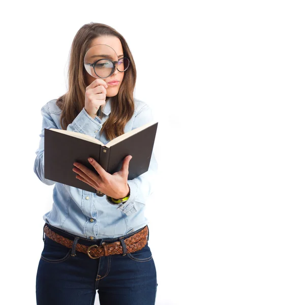 Young woman looking at book by magnifying glass — Stock Photo, Image