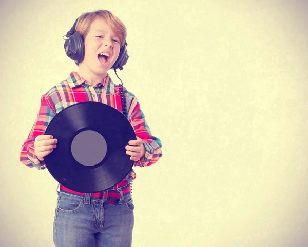 Criança engraçada cantando com fones de ouvido e um vinil — Fotografia de Stock