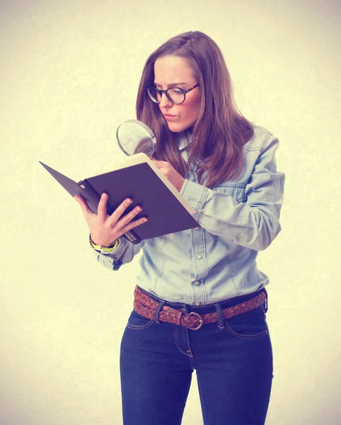 Young woman looking at book by magnifying glass — Stock Photo, Image
