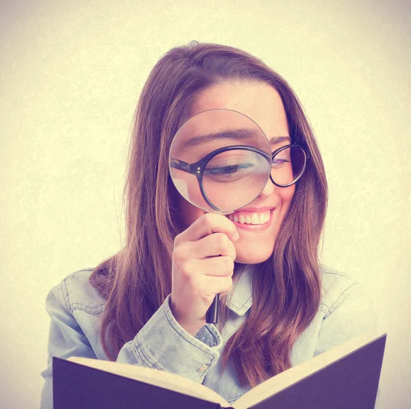 Young woman looking at book by magnifying glass — Stock Photo, Image