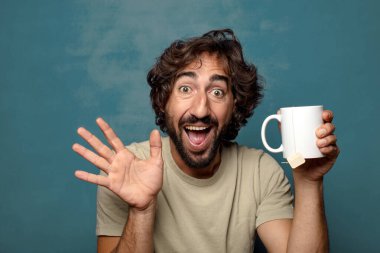 Elinde çay fincanı olan genç, sakallı bir adam.