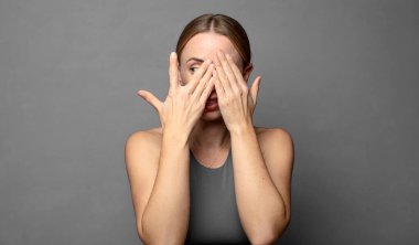 Yüzü ellerle kaplamak, parmaklarının arasından şaşırmış bir ifadeyle yan tarafa bakmak. fitness konsepti