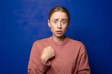 Şok olmuş ve ağzı açık, kendini işaret eden sarışın bir kadın.