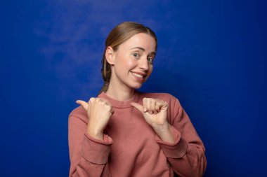 Sarışın kadın neşeyle gülümsüyor ve yan taraftaki fotokopi alanını gösteriyor, mutlu ve tatmin olmuş hissediyor.