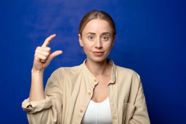 Sarışın kadın elinde bir nesne tutuyor, küçük bir şey gösteriyor, sunuyor ya da reklamını yapıyor.