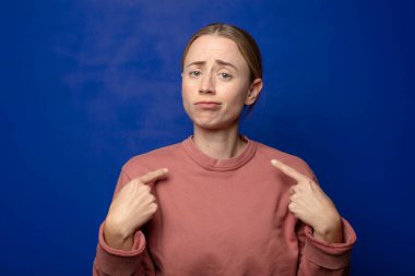 Kötü tavırlı sarışın kadın gururlu ve agresif görünüyor, yukarıyı işaret ediyor ya da elleriyle alay işareti yapıyor.