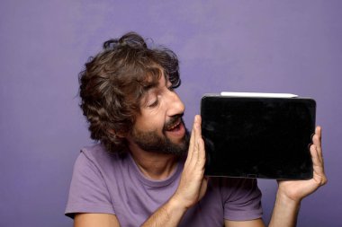 Genç, sakallı, dokunmatik ekranı tutan bir adam.