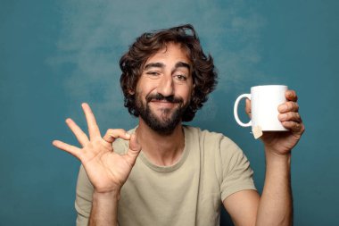 Elinde çay fincanı olan genç, sakallı bir adam.