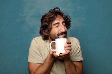 Elinde çay fincanı olan genç, sakallı bir adam.