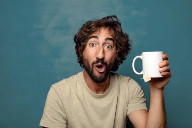 Elinde çay fincanı olan genç, sakallı bir adam.