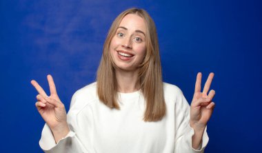 Gülümseyen ve mutlu görünen, dost canlısı ve tatmin olmuş, zafer ya da barış işareti yapan iki elinle