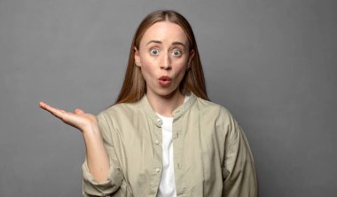 Şaşırmış ve şoke olmuş bir halde, çenesi düşmüş bir objeyi elinde açık bir elle tutarken.