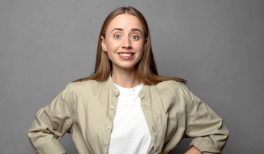 Mutlu bir şekilde gülümsüyor, elleri kalçasında ve kendinden emin, gururlu ve arkadaş canlısı bir tavırla