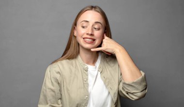 Neşeli bir şekilde gülümsüyor ve telefonla konuşurken kamerayı işaret ediyor.