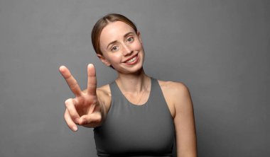 Gülümseyen ve mutlu görünen, kaygısız ve pozitif, tek elle zafer ya da barış işareti yapan. fitness konsepti