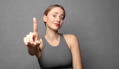 Gururla ve kendinden emin bir şekilde gülümseyerek bir numaralı pozu vererek, bir lider gibi hissederek. fitness konsepti