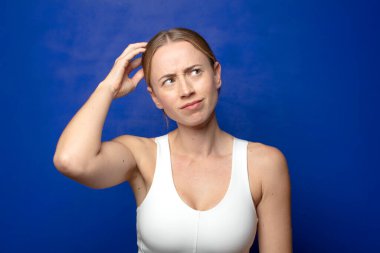 Sarışın kadın şaşkın ve şaşkın hissediyor, kafasını kaşıyor ve yan tarafa bakıyor.