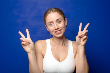 Sarışın kadın gülümsüyor ve mutlu görünüyor, arkadaş canlısı ve tatmin olmuş, zafer ya da barış işareti yapıyor.