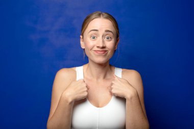 Sarışın kadın mutlu, şaşkın ve gururlu, heyecanlı, şaşkın bakışlarla kendini işaret ediyor.