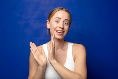 Sarışın kadın kendini mutlu ve başarılı hissediyor. Gülümsüyor ve alkışlıyor. Alkışlarla tebrik ediyor.